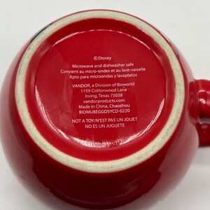 May include: Red ceramic mug with a white rim and handle. The bottom of the mug features text including "Disney", "Microwave and dishwasher safe", and "NOT A TOY/N'EST PAS UN JOUET".