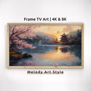 May include: A framed painting of a Japanese temple with a cherry blossom tree in the foreground. The temple is reflected in the water of a lake. The sky is a vibrant orange and pink, suggesting a sunset. The painting is in a light wood frame.
