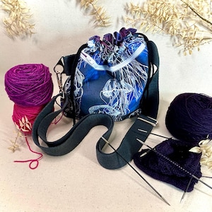 Könnte beinhalten: Eine blaue und weiße Kordeltasche mit einem Quallenmuster und einem schwarzen Riemen. Die Tasche ist mit Garn und Stricknadeln gefüllt.