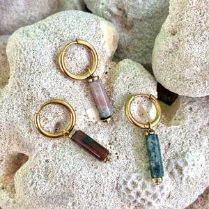 Peut inclure: Trois boucles d'oreilles créoles dorées, chacune dotée d'un pendentif en pierre cylindrique. Les pendentifs présentent des motifs naturels variés dans des tons de rose sourd, de brun profond avec des stries vertes et de vert forêt tacheté.