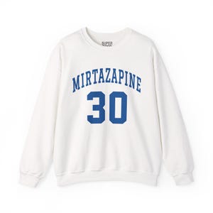 Peut inclure: Sweat-shirt blanc à col rond. Le mot "Mirtazapine" est inscrit en arc de cercle en bleu sur la poitrine, avec le chiffre "30" en dessous. Le mot "SUPER GOOD" est imprimé en petites lettres sur le haut de la poitrine.