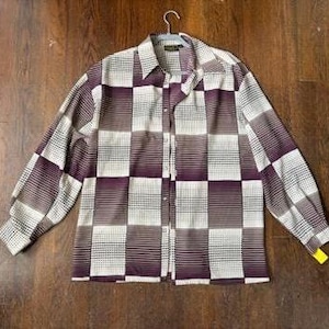 May include: A long-sleeved button-down shirt with a checkered pattern in shades of white, brown, and purple. The shirt is hanging on a hanger and has a classic collar. The fabric appears to be a lightweight material.