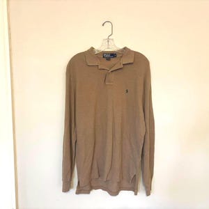 May include: A long-sleeved brown polo shirt with a small embroidered logo on the left chest. The shirt has a button-down collar and a three-button placket.