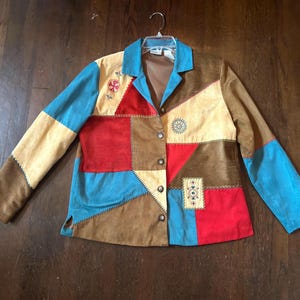 May include: A patchwork jacket in shades of blue, red, tan, and brown. The jacket has a collared neckline and button closure. Decorative stitching and embroidered details are visible on the front.