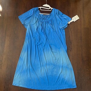 May include: A blue short-sleeved dress with a round neckline and a gathered bodice. The dress has a gradient effect, transitioning from a darker blue at the top to a lighter blue at the bottom. A white tag is attached to the dress.