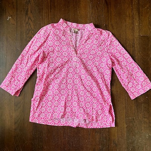 Puede incluir: Una camisa rosa de manga larga con un estampado floral blanco. La camisa tiene cuello en V y mangas tres cuartos. La camisa está hecha de una tela ligera.