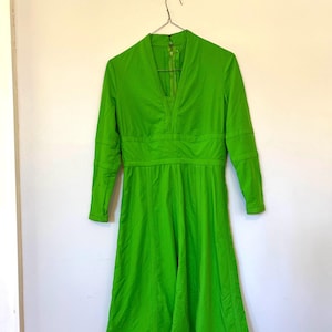 May include: A bright green long-sleeved dress with a V-neckline and a fitted bodice. The dress has a flared skirt and a zipper closure in the back.