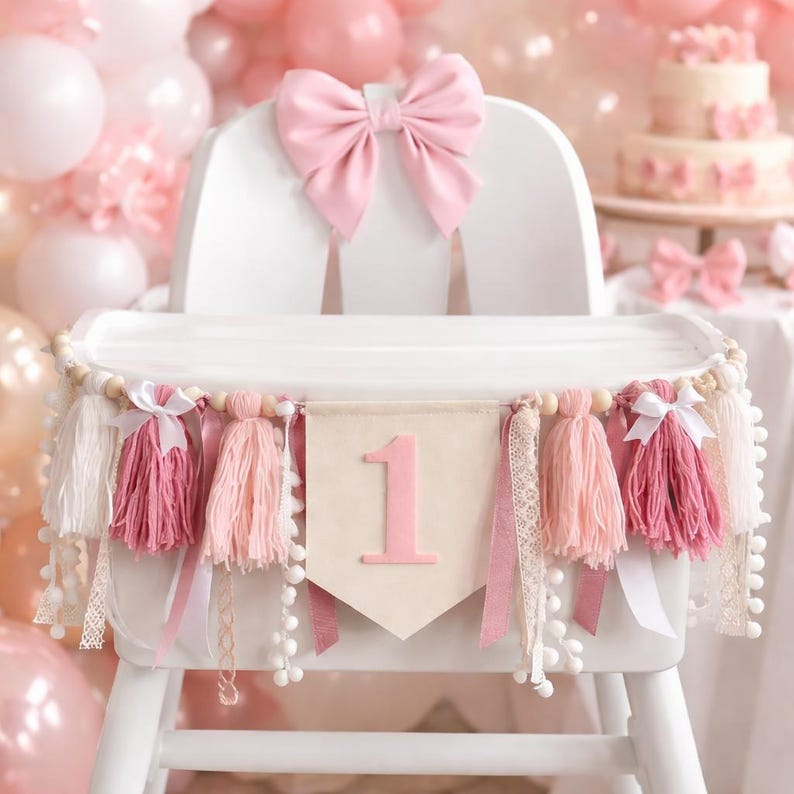 May include: A white high chair decorated for a first birthday celebration. It features a large pink bow, a banner with the number "1", tassels, and ribbons in shades of pink and white. The background includes balloons and a cake.