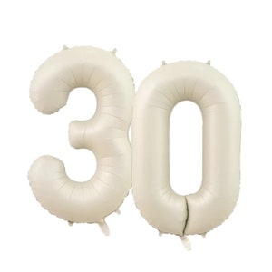 May include: Two large, cream-colored, foil number balloons, forming the number 30.