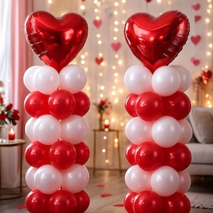 Puede incluir: Dos columnas de globos con globos de papel de aluminio rojos en forma de corazón en la parte superior. Las columnas están hechas de globos redondos rojos y blancos alternados. El fondo incluye luces de hadas y decoraciones de corazón.