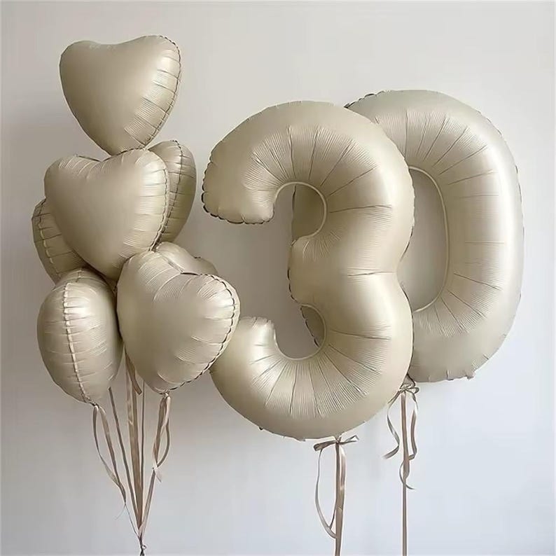 May include: A set of gold foil balloons in the shape of the number 30 and hearts. The balloons are tied together with ribbons.
