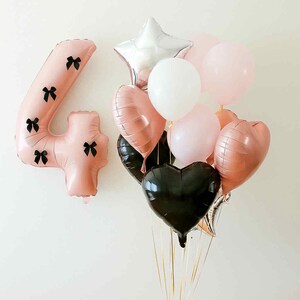 Könnte beinhalten: Eine Sammlung von Ballons in verschiedenen Formen und Farben. Enthält einen großen rosa Ballon mit der Zahl vier und schwarzen Schleifen, herzförmige Ballons in Roségold und Schwarz sowie runde Ballons in Weiß und Rosa. Ein silberner sternförmiger Ballon ist ebenfalls vorhanden.