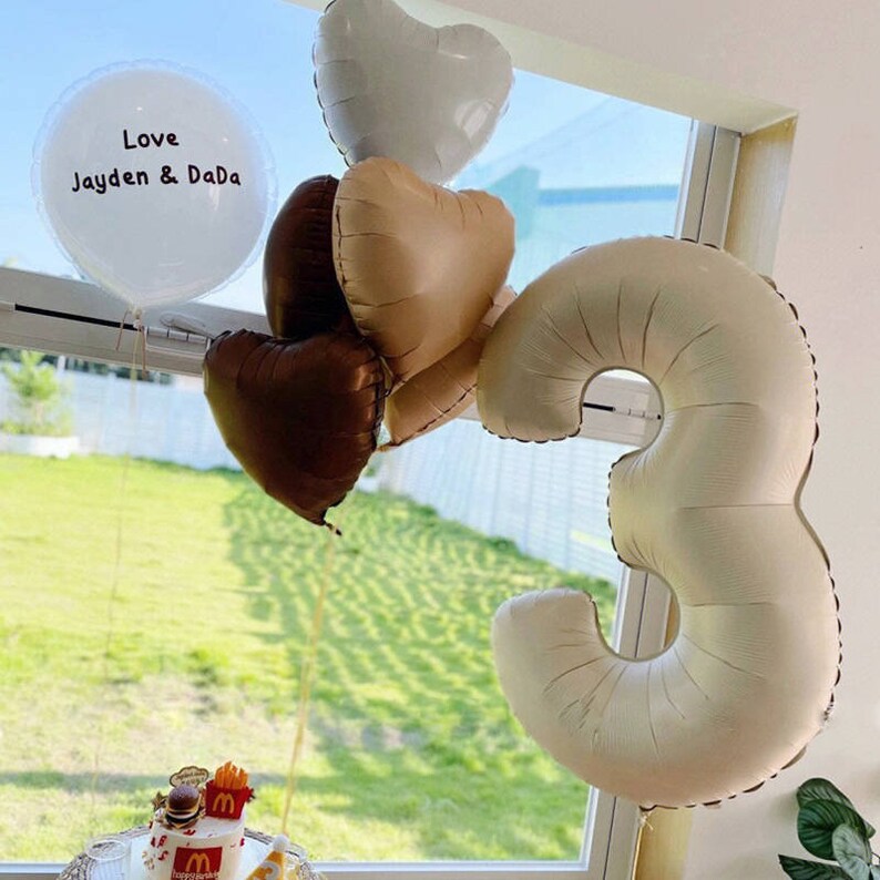 May include: A white balloon with the text "Love Jayden & Dada" and a number 3 balloon in beige. There are also several heart-shaped balloons in beige, brown, and white.