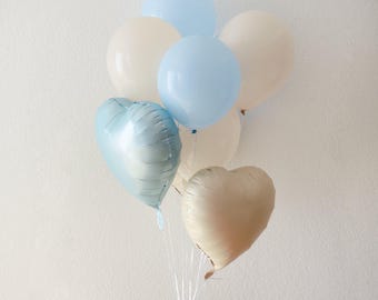 Puede incluir: Un grupo de globos azules y blancos, incluyendo dos globos en forma de corazón, atados juntos con una cuerda transparente.