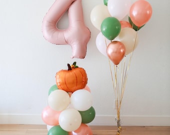 May include: A festive arrangement of balloons and decorations for a fourth birthday celebration. Includes a large, pink number 4 balloon, a pumpkin-shaped balloon, and clusters of white, green, and peach-colored balloons. The balloons are tied with gold ribbons.