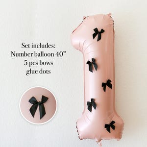 May include: A large, pink number one balloon, approximately 102 cm tall, decorated with five black bows. The image also includes a smaller circular graphic with a single black bow. Text on the left side reads: "Set includes: Number balloon 40" 5 pcs bows glue dots."