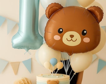 May include: A first birthday celebration featuring a large blue number one balloon, a brown bear-shaped balloon, and a cake. The cake has blue and white stripes and a bear face. Cream, white, and blue balloons add to the festive atmosphere.