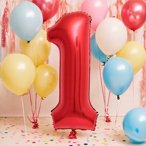 May include: A red foil balloon shaped like the number one surrounded by colorful balloons. The balloons are tied together with white string.