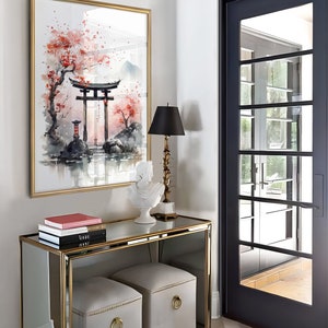 May include: A gold framed mirror with a watercolor painting of a Japanese garden scene. The painting features a red torii gate, a cherry blossom tree, and a small pond. A white ceramic sculpture of a bird sits on a gold mirrored console table with two gray upholstered ottomans. The console table has three books stacked on top of it.