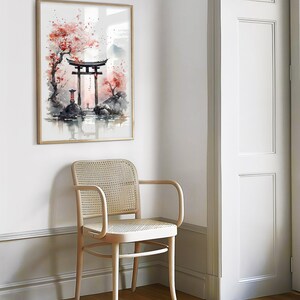 May include: A watercolor painting of a traditional Japanese gate, or torii, surrounded by cherry blossom trees. The gate is red and the trees are pink. The painting is framed in a light wood frame and hanging on a white wall.