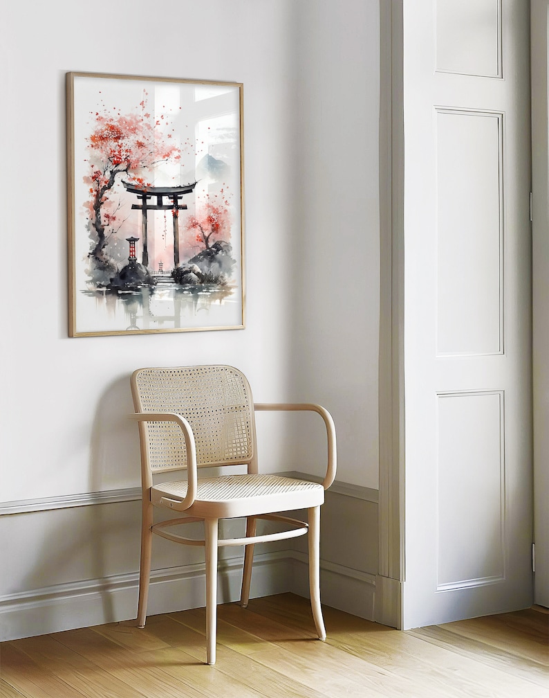 May include: A watercolor painting of a traditional Japanese gate, or torii, surrounded by cherry blossom trees. The gate is red and the trees are pink. The painting is framed in a light wood frame and hanging on a white wall.