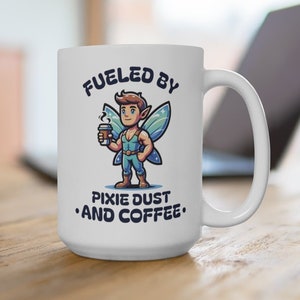 Puede incluir: Taza de cerámica blanca con un asa grande. La taza presenta un dibujo animado de un hada sosteniendo una taza de café, con el texto "Fueled by Pixie Dust and Coffee" en azul. El hada tiene alas azules y viste un atuendo azul.