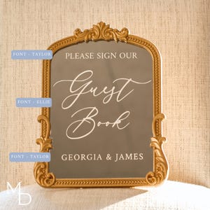 A gold wedding mirror being used as decoration for a wedding entrance table that has a polaroid guest book on it, with the wedding mirror having custom vinyl decal words on it that prompt wedding guests to leave a polaroid and a message as an alternative wedding guest book ideas.