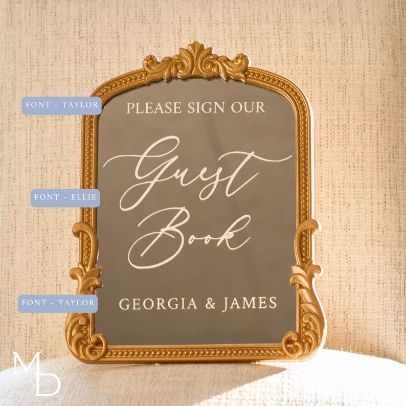 A gold wedding mirror being used as decoration for a wedding entrance table that has a polaroid guest book on it, with the wedding mirror having custom vinyl decal words on it that prompt wedding guests to leave a polaroid and a message as an alternative wedding guest book ideas.