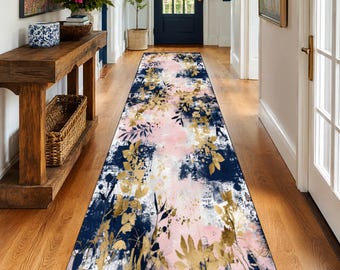 May include: A long, rectangular runner rug with a floral design. The rug features a navy blue background with pink and white accents, and gold-colored leaf and floral patterns. The rug is placed on a hardwood floor in a hallway.