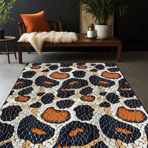 Op de afbeelding: Een rechthoekig vloerkleed met een gedurfd luipaardprintontwerp. Het vloerkleed heeft een patroon van zwarte, oranje en witte vormen, waardoor een textuur, dierlijk geïnspireerde look ontstaat. Het vloerkleed ligt op een houten vloer.