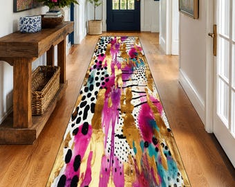 May include: A colorful runner rug with an abstract design. The rug features a mix of gold, pink, black, white, and teal colors. The pattern includes brushstrokes, polka dots, and other artistic elements. This decorative rug is suitable for hallways and entryways.