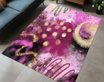 Op de afbeelding: Een rechthoekig vloerkleed met een abstract ontwerp. Het heeft een mix van roze, magenta, zwart en goud. Het ontwerp bevat inktachtige wervelingen, stippen en penseelstreken. Het kleed ligt op een grijze tegelvloer.