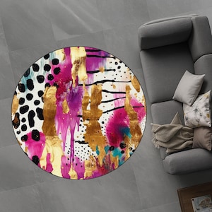 May include: A circular rug with an abstract design. The rug features a white base with gold, black, pink, purple, and teal accents. The design incorporates brushstrokes, polka dots, and drips, creating a vibrant look.