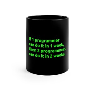 Op de afbeelding: Zwarte koffiemok met groene tekst die zegt: "Als 1 programmeur het in 1 week kan doen, dan kunnen 2 programmeurs het in 2 weken doen."