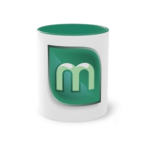 May include: White ceramic mug with a green rim and a green leaf-shaped logo with the letter "m" in a light green color.