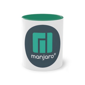 Puede incluir: Taza de cerámica blanca con borde verde y un círculo negro con un logotipo verde que dice "manjaro" en texto blanco.