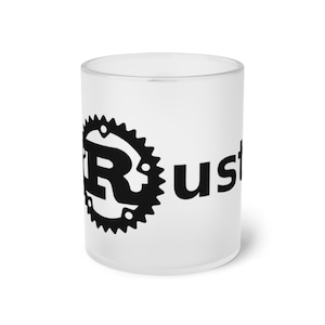 Puede incluir: Taza de vidrio esmerilado blanco con un logotipo de Rust negro que presenta un engranaje y la letra R. El texto "Rust" está impreso en negro debajo del logotipo.