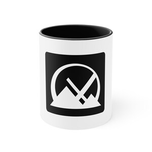 Könnte beinhalten: Weiße Keramiktasse mit schwarzem Rand und einem schwarzen Grafikmotiv eines Kreises mit einer Bergkette darin und einer diagonalen Linie über dem Kreis. Das Motiv befindet sich in einem schwarzen Quadrat.