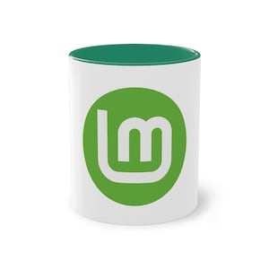 Könnte beinhalten: Weiße Keramiktasse mit grünem Rand und einem grünen Kreislogo mit dem Buchstaben "m" in der Mitte. Das Logo ist das Logo des Betriebssystems Linux Mint.