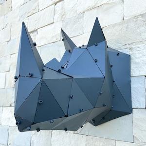 Peut inclure: Sculpture de tête de rhinocéros en métal noir avec un design géométrique. La sculpture est composée de nombreux petits triangles et est fixée au mur à l'aide de vis.