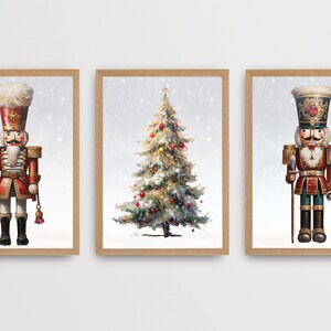 May include: Three framed prints featuring a Christmas tree and two nutcracker soldiers. The nutcracker soldiers are wearing red and gold uniforms with white fur hats. The Christmas tree is decorated with red ornaments and has a white snowy background.