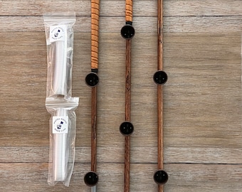 May include: Three wooden golf club holders with a leather strap and a silver golf club head. The holders have black cups for golf balls. The holders are arranged in order of size, with the largest on the left and the smallest on the right. A package of white plastic golf ball cups is on the left side of the image.