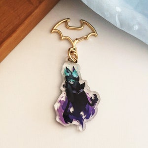 May include: A black and purple character keychain with a bat-shaped metal clasp. The character has a blue and green design on its head and is surrounded by purple flames.
