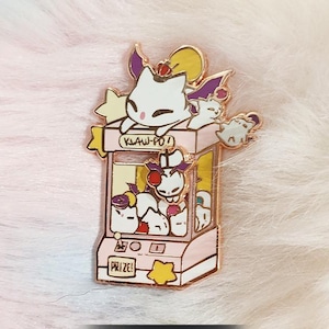 May include: A gold-colored pin featuring a pink claw machine with cartoon cat characters. The machine has the text "KLAW-PO!" and "PRIZE!" on it. The pin is set against a fluffy, multicolored background.