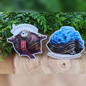 May include: Two stickers on a wooden surface. One features a cartoon character with a sun-like headdress and the text "wheeeeeeeeee". The other sticker has a blue and black design with the text "whoooooooo".