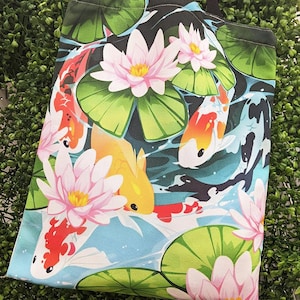 Puede incluir: Una bolsa de lona negra con un diseño colorido que presenta peces koi nadando en un estanque con nenúfares y flores.