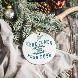 Op de afbeelding: Witte keramische ornament met een blauwgroen ontwerp. De ornament heeft de tekst "Here Comes The Tush Push" met een voetbalafbeelding.