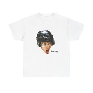 May include: White t-shirt featuring a graphic of a person wearing a black hockey helmet with the text "boring." The helmet has the brand name "CCM" on it. The person is sticking their tongue out.