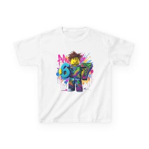 May include: White t-shirt featuring a colorful graphic of a Roblox-style character holding the numbers 6 and 7. The design includes a smiley face and vibrant paint splatter effects, suitable for a birthday celebration.