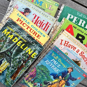 May include: A collection of vintage Little Golden Books with colorful covers. Titles include "Animal Book," "Heidi," "Madeline," and "Paul Revere." The books are stacked on a wooden surface, showcasing their classic illustrations and text.